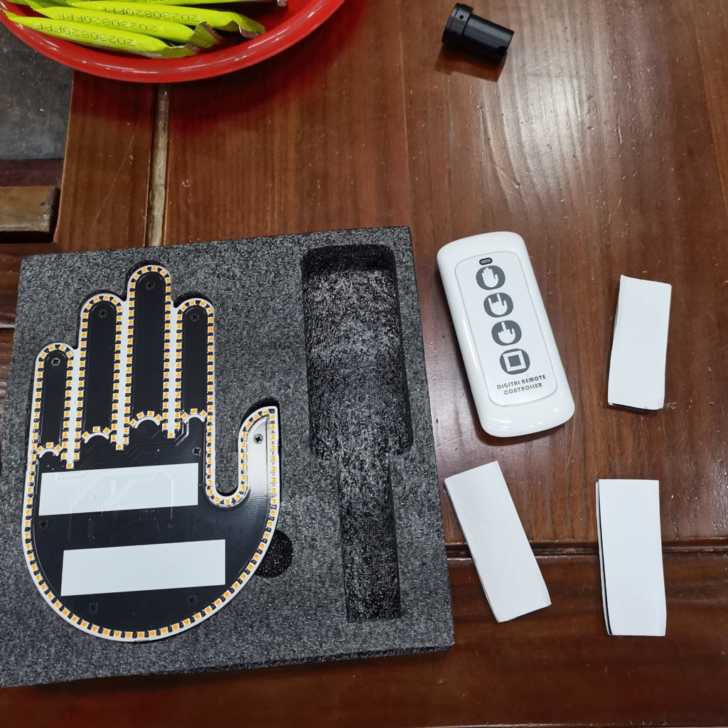 Hand-shaped electronic component on a wooden surface with remote control and batteries.